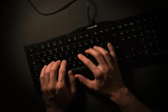 Top-down view of a person’s hands typing on a black mechanical keyboard in a dimly lit room.