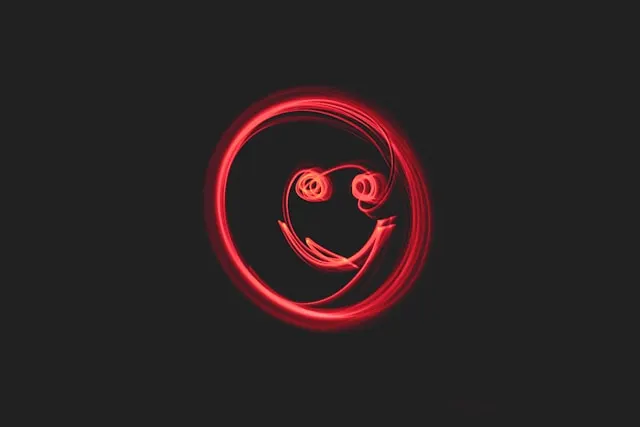 A long-exposure light painting created with red light trails against a black background, forming a crude, glowing smiley face inside a circle.